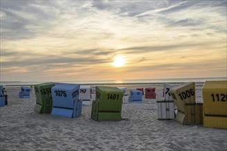 Various colourful beach chairs on a sandy beach at sunset with a view of the sea, many colourful