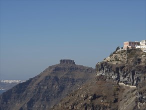 A prominent peak with houses standing high on the steep cliffs of Santorini, under a clear sky,