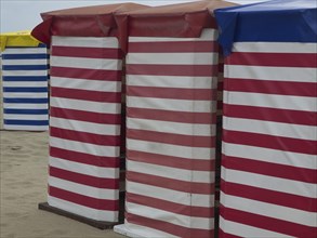Striped beach huts in red-white and blue-white on the sandy beach, beach chairs and beach tents by