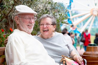 Laughing senior adult couple enjoying the carnival from the outdoor bench