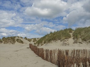 Scenic dune landscape with a wooden fence under a cloudy sky, beach and dunes with grass and a
