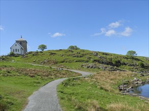 Church in the distance with hiking trail, hilly landscape and blue sky with clouds, old stone