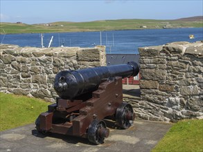 Old cannon in front of a stone wall with a view of the sea and green hills in the background, old