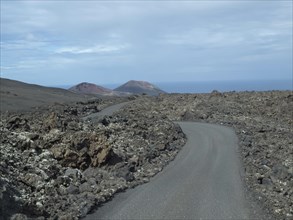 A winding tarmac road through a volcanic landscape, surrounded by lava and rocks under a cloudy