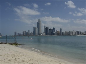 A sandy beach with a view of the skyscrapers of a modern city by the sea under a cloudy sky,