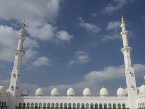 Mosque with two minarets and a row of white domes against a blue sky, beautiful mosque with white