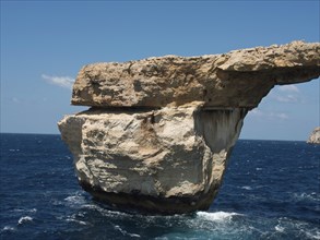 Massive rock arch towers over the sea, surrounded by cliffs under clear blue skies, many historic