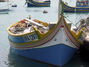 A fishing boat with nets and equipment is moored in a coastal town on the water, many colourful