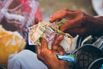 Older hands counting weathered paper Indonesian currency called Indonesian Rupiah, suggesting a