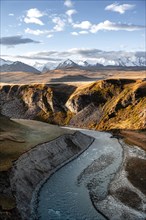 Mountain stream Sary Jaz, behind Glaciated and snow-covered mountains, autumnal plateau with yellow
