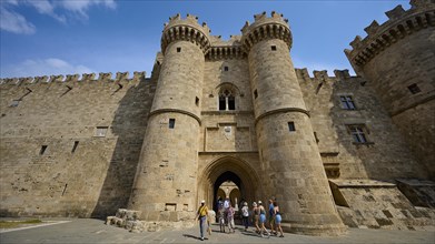Super wide angle shot, several people admiring a mighty castle with watchtowers and blue sky in the