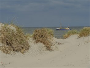 Sand dunes with grass and a boat on the sea under a cloudy sky, dune with dune grass and a boat by