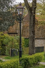High black street lamp next to a tree in front of houses with tiled roofs, old houses with green