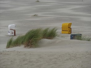 Two beach chairs, one yellow and one white, stand in the dunes on the deserted beach, colourful