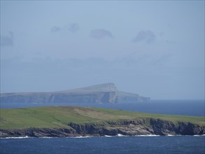Grassy cliffs jutting into the azure sea with a distant island in the background, green meadows on