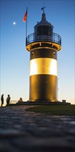Black and white lighthouse, called 'Kleiner Preusse', stands illuminated at night shortly after