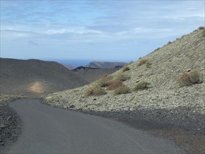 A tarmac road winds its way through overgrown, barren hills under a slightly cloudy sky, barren