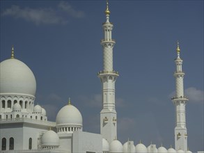 Large white mosque with magnificent domes and slender minarets against a blue sky, large mosque