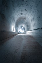 A long tunnel with cold concrete walls and a straight structure that looks industrial and sterile,