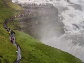 Tourists hike along a path next to an impressive, misty waterfall, Iceland, Europe