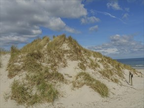 High sand dunes with grass, above a sky with some clouds, dunes on an island with a blue boat and a