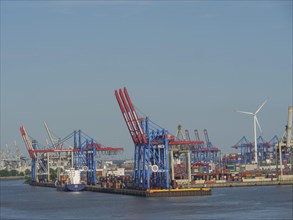 Harbour with cranes, containers and a wind turbine under a blue sky, cranes and ships in a harbour,