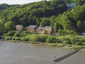 Old industrial buildings embedded in green hills and trees on the river bank, green bank on a river