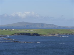 View of the tranquil coastal landscape with houses and hills in the background, green meadows by a