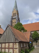 Half-timbered house and high church tower against a cloudy sky with red tiled roofs and trees,