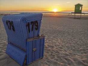 Sunset on the beach with a blue beach chair and a golden sky over the sea, beautiful sunset on the