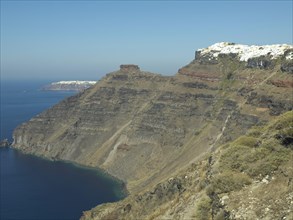 A panorama of the coast of Santorini with high cliffs, whitewashed houses and the vast sea in the