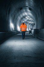 A worker in a safety waistcoat walks through an illuminated, futuristic tunnel with concrete walls,