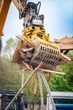 Hydraulic grab on an excavator lifts piles of wood against a green background on a construction