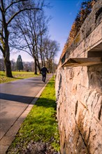 A man walks along a steep wall in a green park in sunny weather, spring, Nagold, Black Forest,