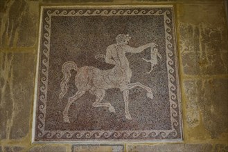 Antique mosaic with a centaur holding a rabbit, surrounded by decorative patterns, outdoor area,