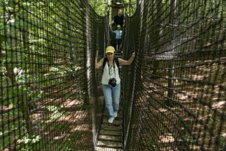 Sporty woman, tourist with camera in treetop path, suspension bridges, ropes, nets, beech forest,