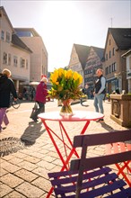 A table with a bouquet of flowers in a busy urban outdoor area in sunny weather, spring, Nagold,