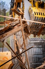 Machine arm of an excavator with hydraulic grab lifting pieces of wood on a construction site,