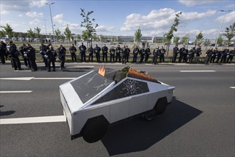 A Cybertruck cardboard model in front of the factory premises guarded by police officers during the