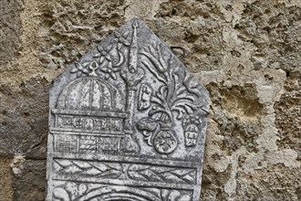 Historical tombstone with detailed reliefs and old lettering, depiction of a mosque, outdoor area,