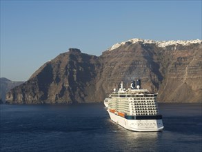 A large cruise ship approaches the imposing cliffs of Santorini, with white houses adorning the