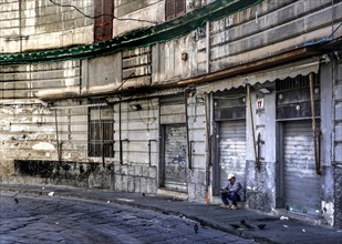 A man sits in front of a closed shop in the historic centre of Naples, 02/05/2024, Naples, Italy,