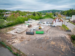 A construction site with demolished material and containers, surrounded by houses, green trees and