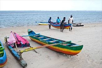 Beach attendants carrying a canoe to take it away from the sea, beach on the Indian ocean,