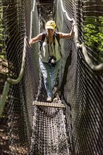 Sporty woman, tourist with camera in treetop path, suspension bridges, ropes, nets, beech forest,