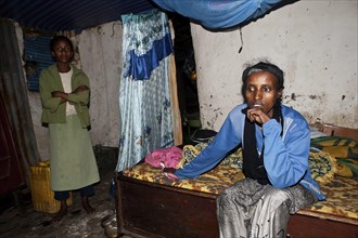 Portrait of a poor woman suffering from aids. She is sitting on her bed at home, her daughter is