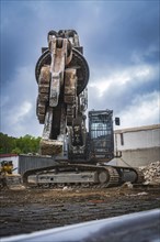 An excavator with a grab arm sits on a construction site with demolished buildings and bricks,