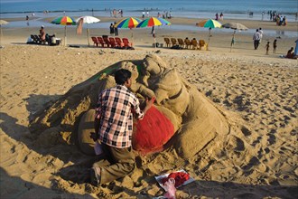 Sand artist sculpting a sand sculpture, sculpture representing a couple of lovers, beach at Puri,