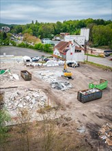 A construction site with demolished material and containers, machines and surrounded by houses and