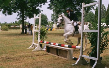 Young rider jumping over a barrier during a competition, equestrian sport in France